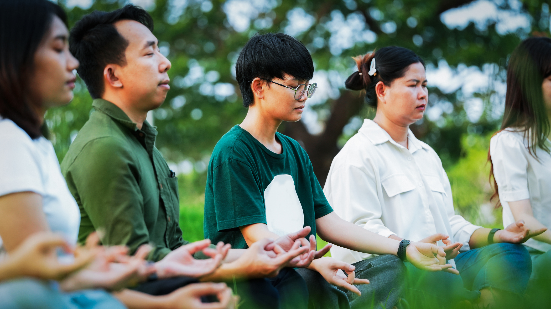 Group of diverse Asian people practicing meditation together in a green park for mental health and wellness lifestyle concept