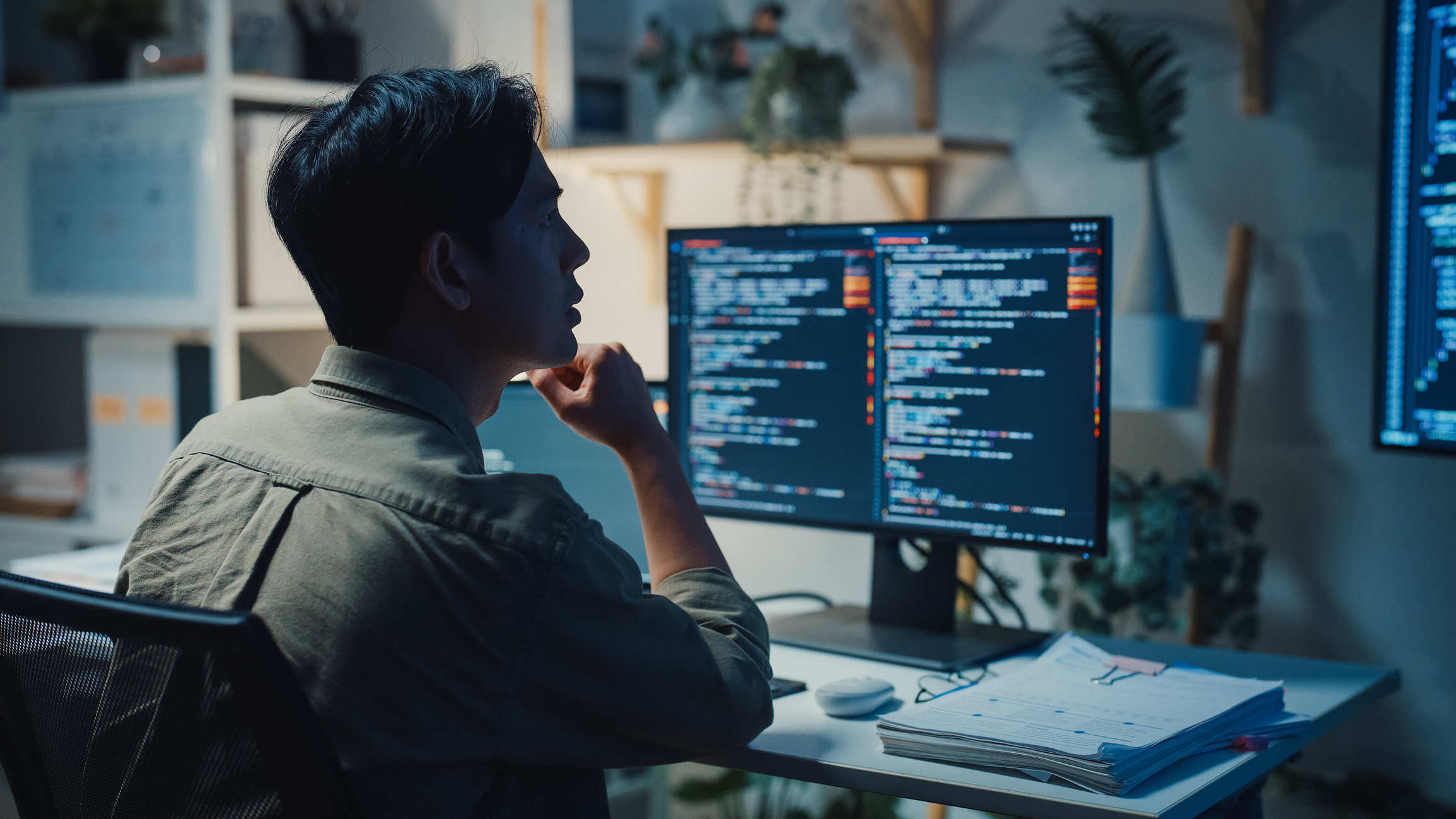 Young male IT professional examines a computer language working late at night in office. Artificial intelligence data science, python programming, network security concepts.